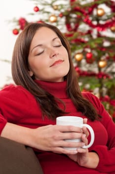 Brown hair woman relaxing with cup of coffee in front of Christmas tree