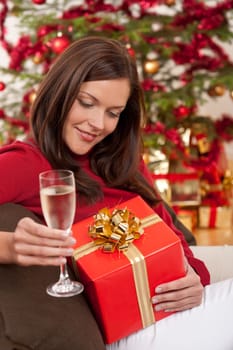 Smiling woman with Christmas present and glass of champagne in front of tree