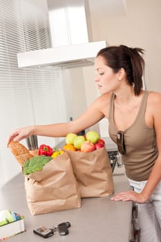 Young woman with groceries in the kitchen with shopping bags