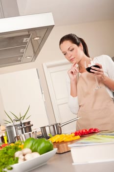 Young woman cooking in the kitchen and holding glass of red wine