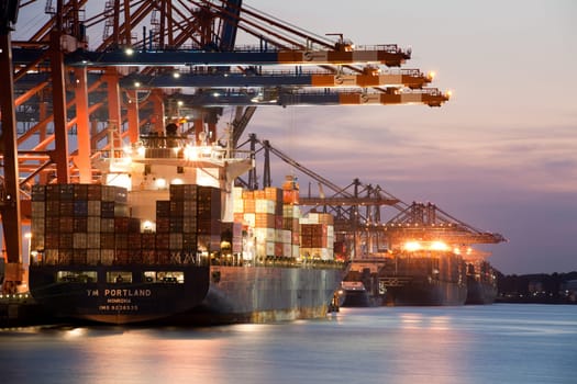 Large container ships - freighters being loaded in port at night. Hamburg, Germany.