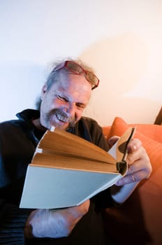Elderly man with beard,glasses and book reading on sofa at home