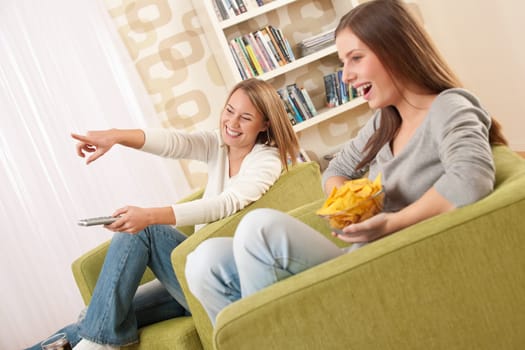 Students - Two female teenager watching television and eating crisps in modern lounge