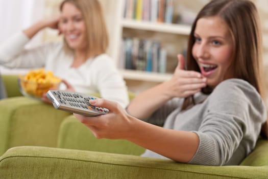 Students - Two smiling female teenager watching television in modern living room, focus on remote control