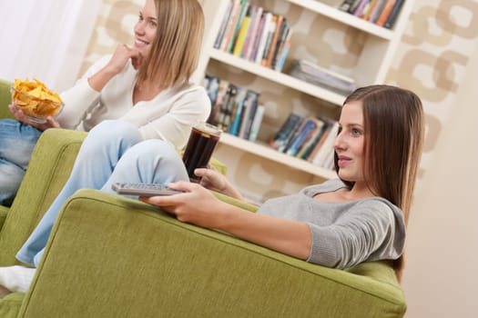 Students - Two female teenager watching television and eating crisps in modern lounge