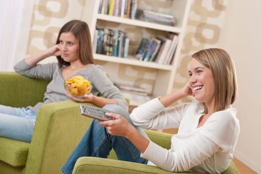 Students - Two female teenager watching television and eating crisps in modern lounge