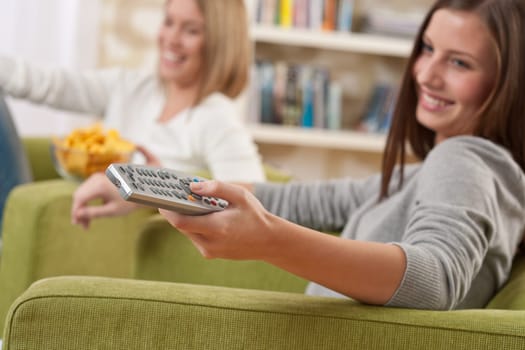 Students - Two smiling female teenager watching television in modern living room, focus on remote control
