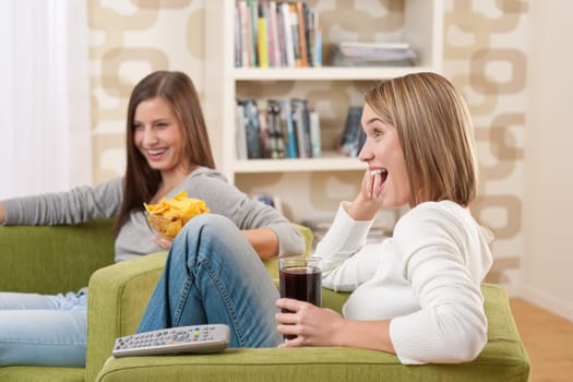 Students - Two smiling female teenager watching television together, eating crisps