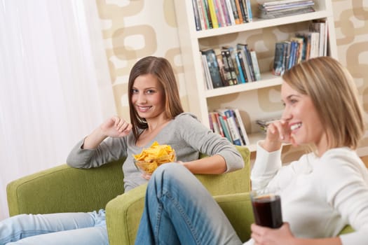 Students - Two smiling female teenager watching television together, eating crisps