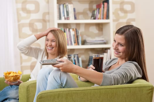 Students - Two female teenager watching television and eating crisps in modern lounge