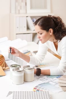 Young female interior designer at office with paint and color swatch