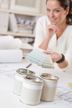 Young female interior designer working at office with color swatch and can of paint