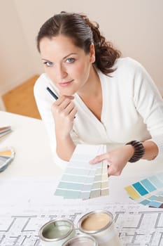 Young female interior designer working at office with color swatch and can of paint