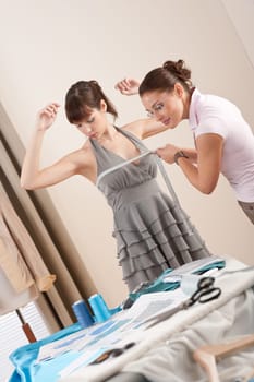 Female fashion designer measuring model for fitting gray dress, taking measurement