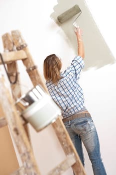 Home improvement: Cheerful woman with paint roller and ladder painting wall