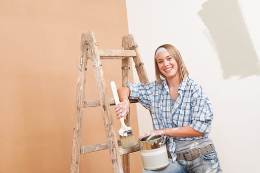 Home improvement: Smiling woman with paint and brush painting wall