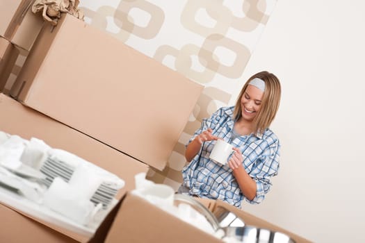 Moving house: Happy woman with box holding cup of coffee in new home