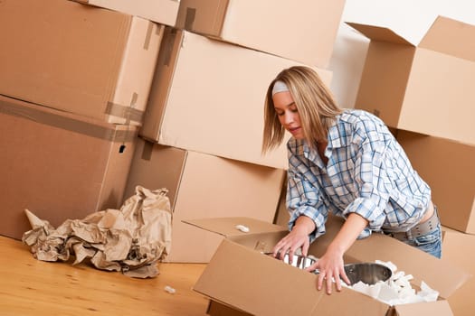 Moving house: Happy woman unpacking box in new home, kitchen, pots and pans
