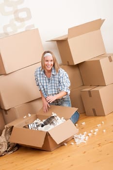 Moving house: Happy woman unpacking box in new home, kitchen, pots and pans
