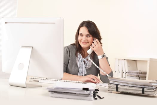 Attractive secretary on phone at office in front of computer screen