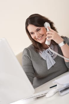 Attractive executive woman on phone at office watching computer screen
