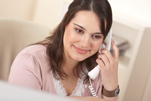 Portrait of young businesswoman on phone at office in front of computer screen