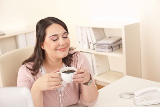 Young business woman enjoying coffee at modern office sitting at computer