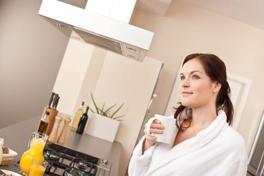 Young woman in bathrobe enjoying cup of coffee in kitchen
