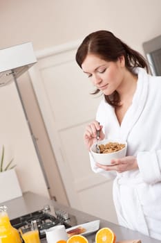 Happy woman in bathrobe eating healthy cereals for breakfast in kitchen