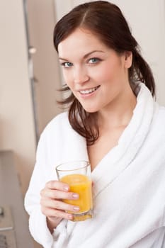Young woman in bathrobe drink orange juice for breakfast in kitchen