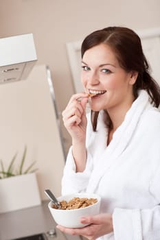 Happy woman in bathrobe eating healthy cereals for breakfast in kitchen