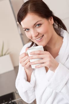 Young woman in bathrobe enjoying cup of coffee in kitchen