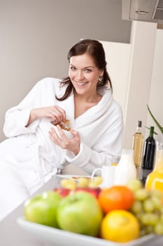 Happy woman in bathrobe eat cereals for breakfast in kitchen