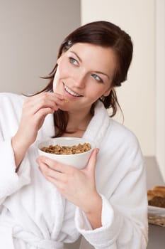 Happy woman in bathrobe holding bowl with cereals for breakfast