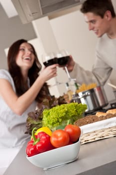 Young couple drinking red wine in kitchen, focus on bowl with vegetable