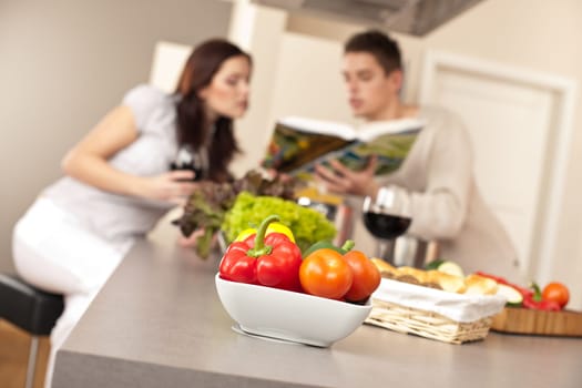 Young couple in kitchen choosing recipe from cookbook drinking red wine