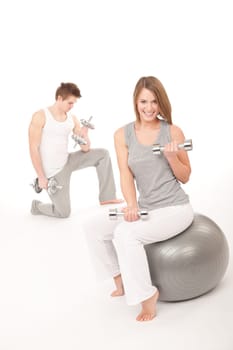 Fitness - Young healthy couple training with weights and ball on white background