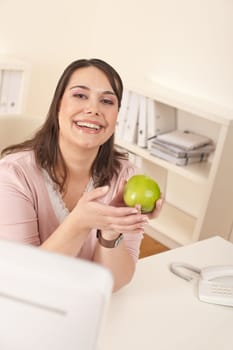 Young happy businesswoman holding apple at office having snack