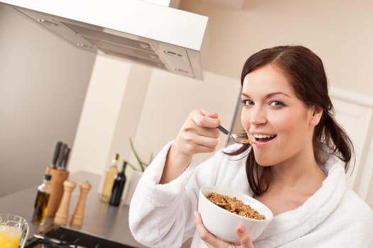 Happy woman in bathrobe eating healthy cereals for breakfast in kitchen