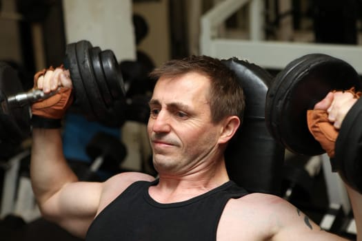 training dumbbells in gym. Male lifting weights for upper body strength building pecks, shoulders and biceps