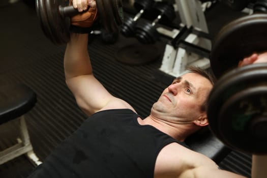 training dumbbells in gym. Male lifting weights for upper body strength building pecks, shoulders and biceps