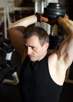 training triceps with free weights. Male lifting dumbbell over head building muscle strength