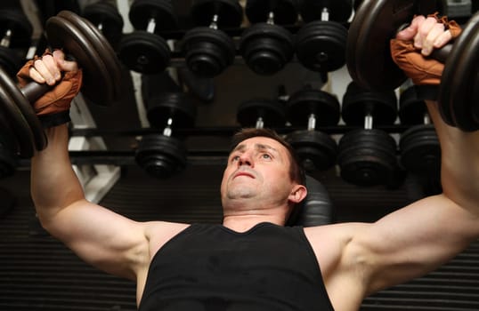 training dumbbells in gym. Male lifting weights for upper body strength building pecks, shoulders and biceps