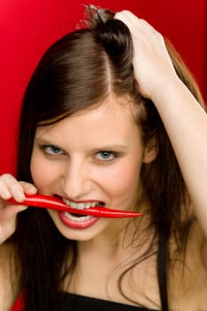 Chili pepper - portrait young woman bite red spicy veg on red background