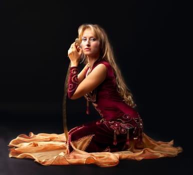 Beauty arabian dancer sit with saber on black background