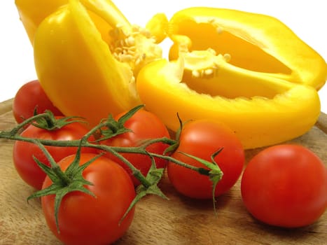 Halved yellow peppers and tomatoes on wooden plate with knife