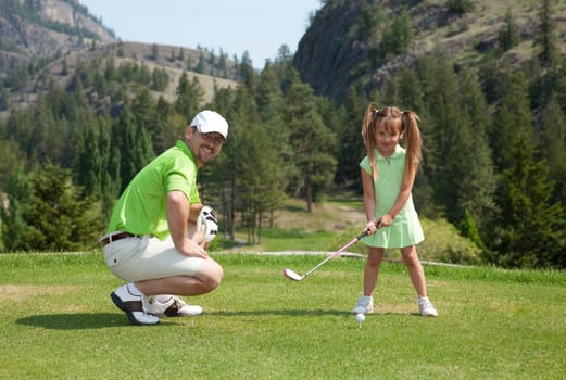 Outdoor photo of father and youngster daughter on golf course.