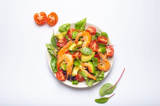 Healthy salad with grilled shrimps, avocado, cherry tomatoes and green leaves on white plate isolated on white background top view. Clean eating, nutrition and dieting concept..