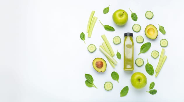 Bottle of green smoothie surrounded by green fruit and vegetables: apples, avocado, spinach, celery, cucumber on white simple background top view. Diet, healthy nutrition, detox, copy space