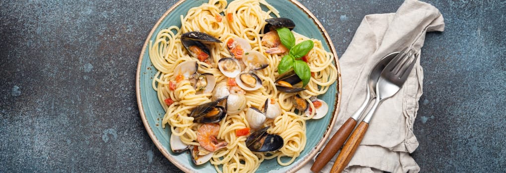 Italian seafood pasta spaghetti with mussels, shrimps, clams in tomato sauce with green basil on plate on rustic blue concrete background overhead. Mediterranean cuisine